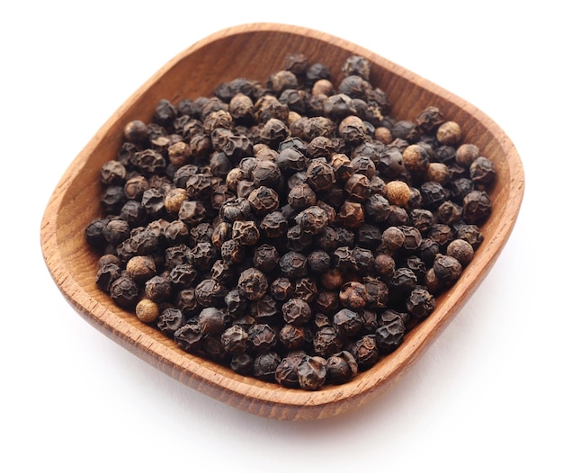 Black peppers on wooden bowl over white background