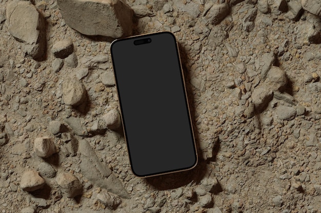 Foto un telefono nero steso a terra con rocce sullo sfondo.