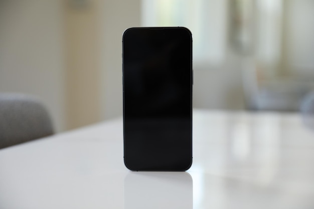 A black phone with a blank screen sits on a white table.