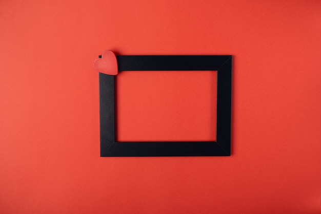 Black photo frame with red wooden heart on red. Valentine's Day concept.