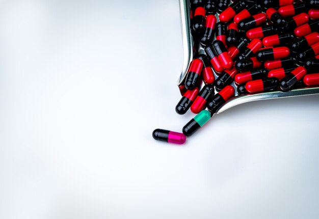 Черно-розовые, черно-зеленые и черно-синие капсулы для таблеток и поднос с лекарственными препаратами Антибиотики, лекарственная устойчивость. Противомикробные капсульные таблетки. Аптека фон. Фармацевтическая индустрия. Концепция генной мутации.