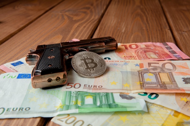 Black pistol, euro and coin in the form of bitcoin