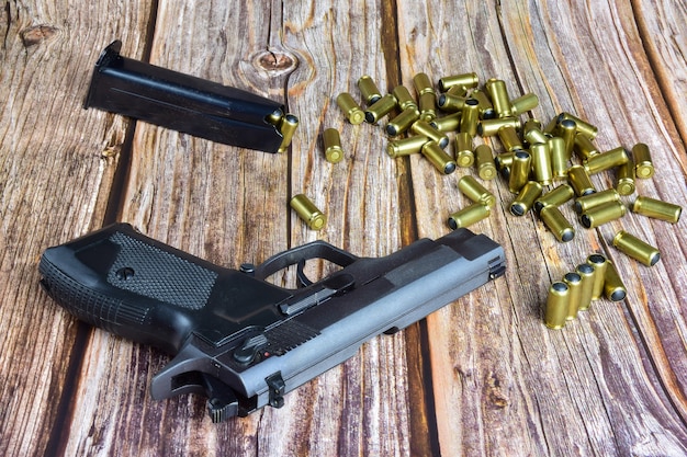 A black pistol and several traumatic cartridges lie on old brown wooden boards.