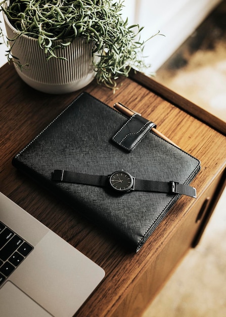 Black planner on a wooden desk by a laptop