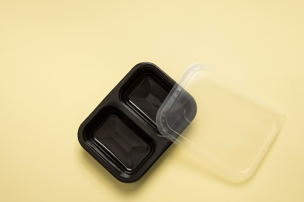 Black plastic container for food delivery service in a yellow background