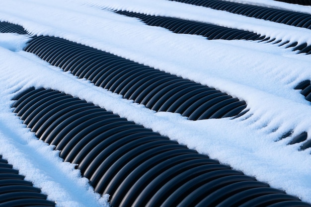 Black plastic corrugated drain pipes covered by the snow