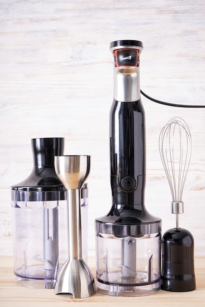 Black plastic electrical hand blender and accessory on the wooden background, verticall