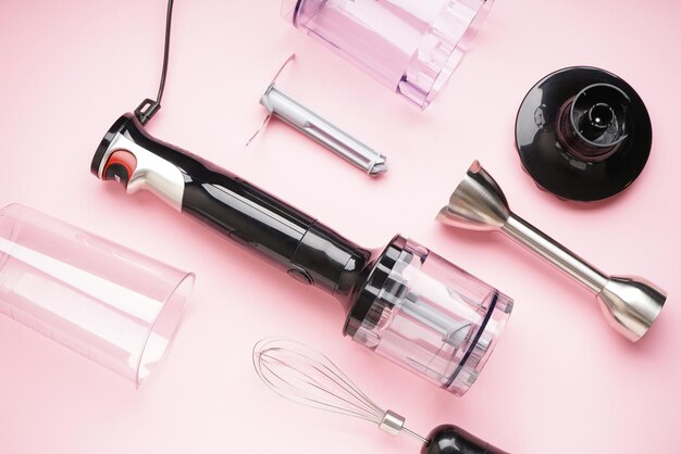 Photo black plastic electrical hand blender with stainless steel body and accessory on the pink background. flat lay.