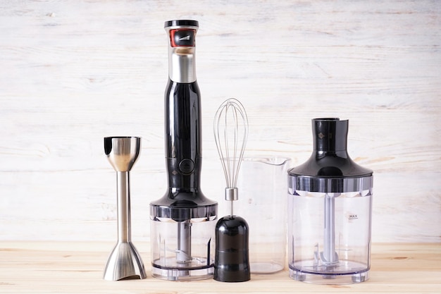 Black plastic electrical hand blender with stainless steel body and accessory on a wooden background.