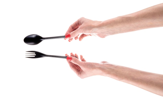 白い背景に分離された女性の手で黒いプラスチックのフォークとスプーン