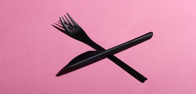 Black plastic knife and fork on pink pastel surface