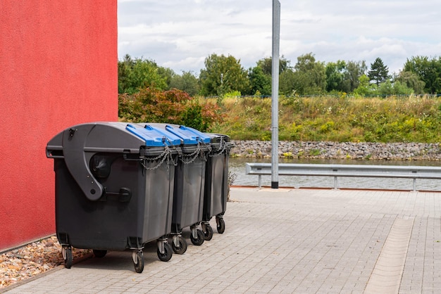 Black plastic trash cans closed on a chain stand near a large red building