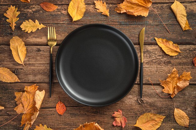 A black plate and cutlery among autumn leaves on a wooden background