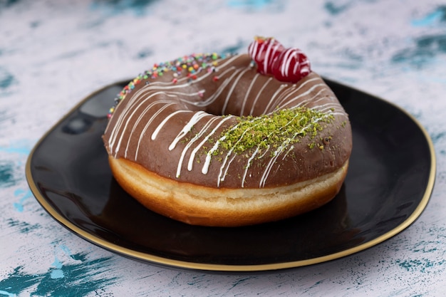 Black plate of delicious chocolate donut with cherry and colorful sprinkles . 