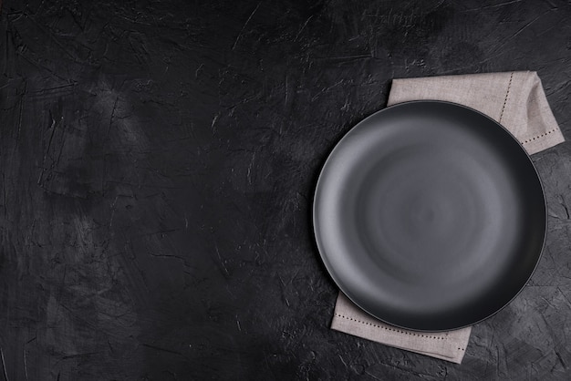 Black plate, linen napkin on black stone table top view. Table setting.