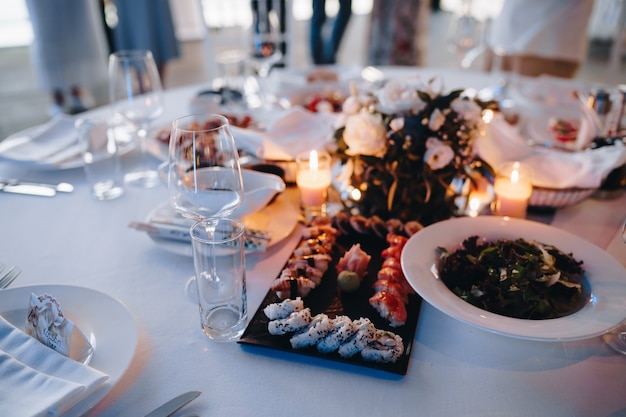 접시에 샐러드와 함께 테이블에 흰색 식탁보에 초밥과 롤을 제공하는 블랙 플레이트