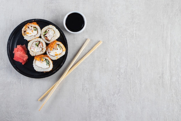 Black plate of sushi rolls with chips and crab on stone background. 