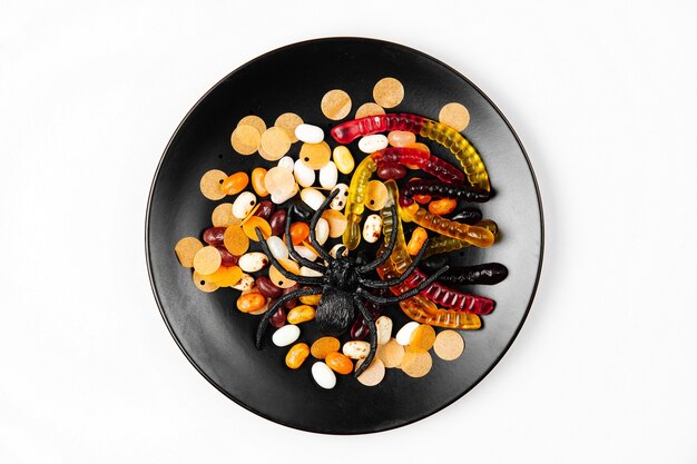 Black plate with colorful candy. Trick or Treat, concept for Halloween. Flat lay, top view