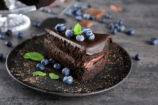 Black plate with delicious chocolate cake on grey background