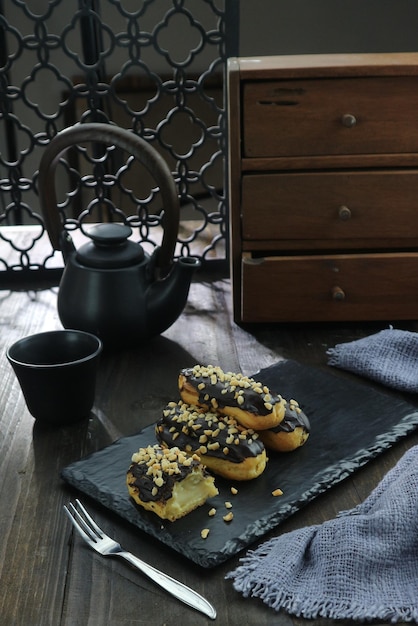 A black plate with donuts on it and a teapot on the table.