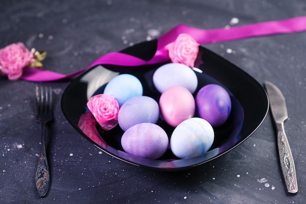 A black plate with multicolored painted Easter eggs on a dark neonstyle table