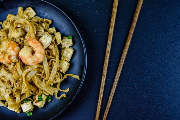 Black plate with pad thai and chopsticks on a slate board Top view