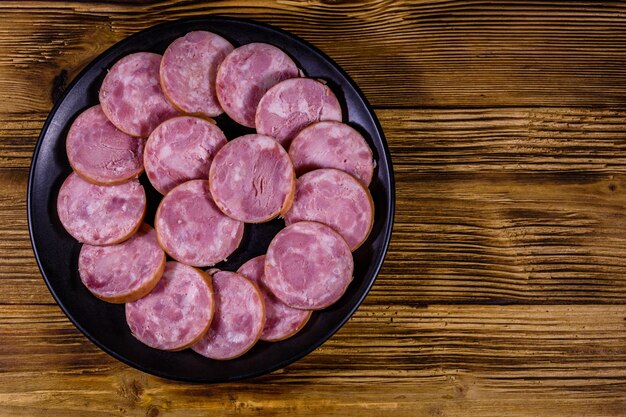 Black plate with sliced sausage on a wooden table Top view