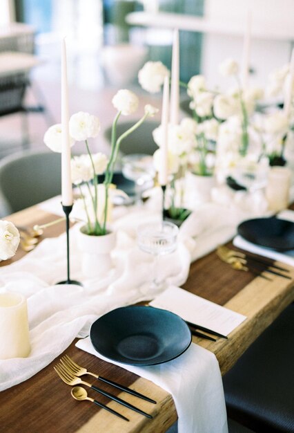 Black plates stand on white napkins next to bouquets of flowers and candles on the festive table