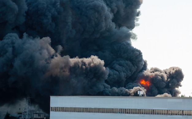 Black plumes of smoke from an accidental toxic industrial fire as seen from a behind a factory building.