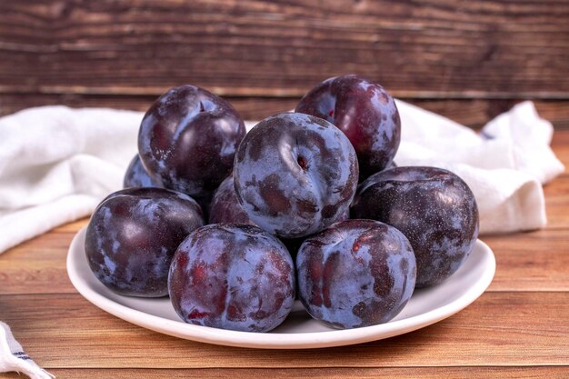 Black plums on wood background Pile of black plums on a white serving plate close up