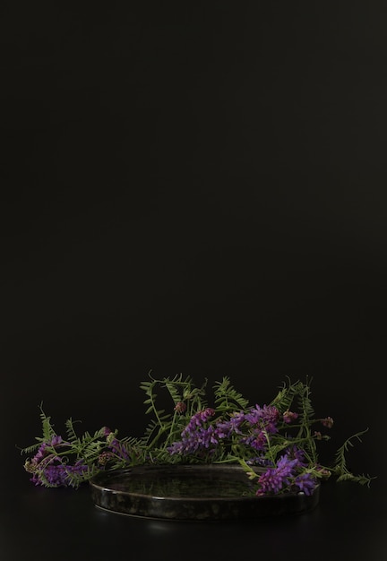 Black podium on the black background with flowersPodium for product cosmetic presentationMock up