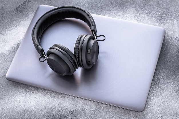 Black portable headphones on a purple metal notebook on grunge gray background. Closed laptop with earphones on grey backdrop.