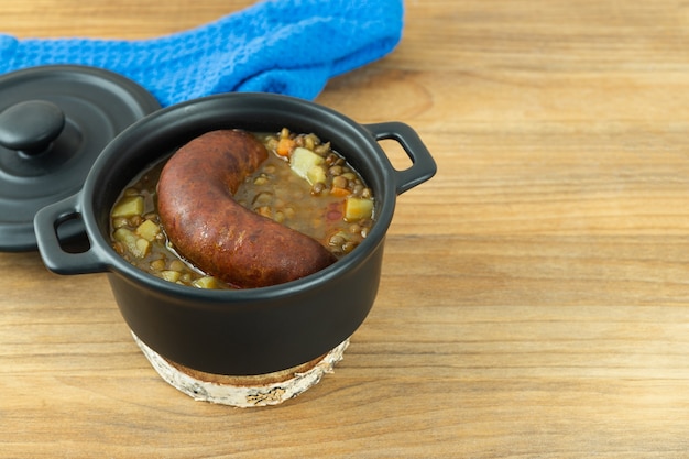 Black pot with lentils and sausage on wooden background. Copy space.