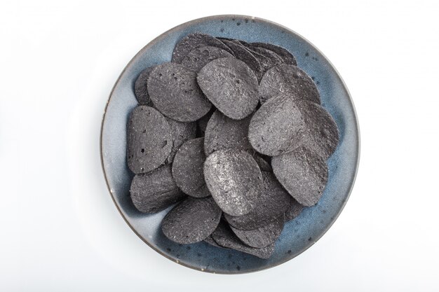 Black potato chips with charcoal on a blue ceramic plate isolated on white background