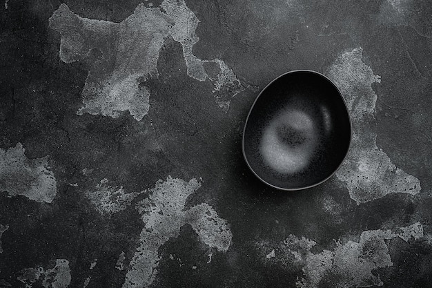 Black pottery bowl with copy space for text or food with copy\
space for text or food top view flat lay on black dark stone table\
background