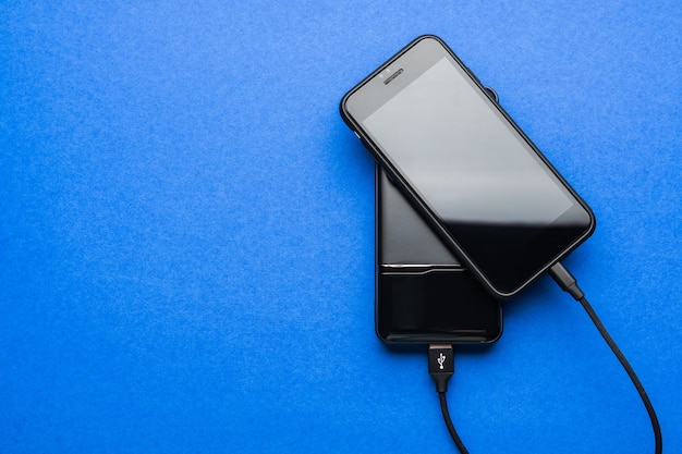 Black Power bank charges smartphone isolated on blue surface