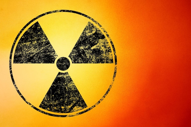Фото Черный предупреждающий знак радиоактивной опасности закрашен на гранжевом желтом и красном фоне с копировальным пространством
