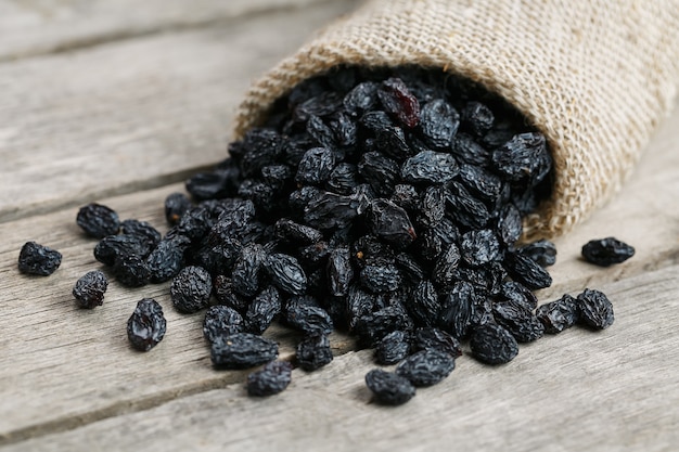 Black raisins in burlap bag over wooden gray table