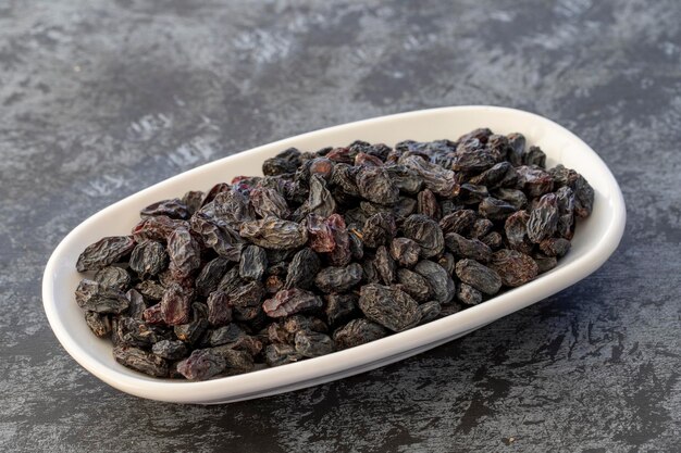 Black raisins on plate on dark background