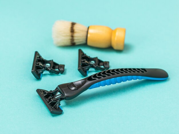 Black razor with two replacement blades and a shaving brush for shaving on a blue background. Set for care of a man's face.