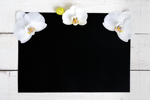 Il rettangolo nero formato a4 e uno sfondo in legno bianco decorato con fiori di orchidea bianchi