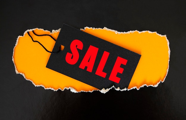 Photo a black rectangular clothing tag rests on torn black paper. yellow background. sale concept.