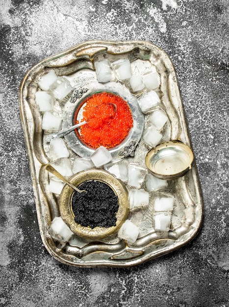 Black and red caviar in bowls on old tray.