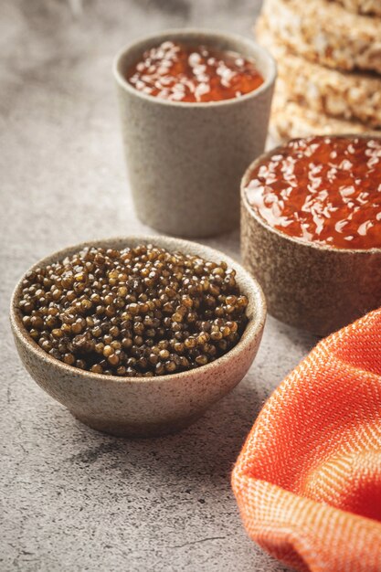 Black and red caviar in bowls, snacks on a gray concrete table