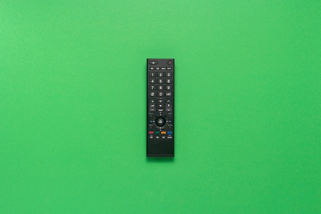 Photo black remote control on a green background. the concept of television, movies, tv shows, sports. flat lay, top view.