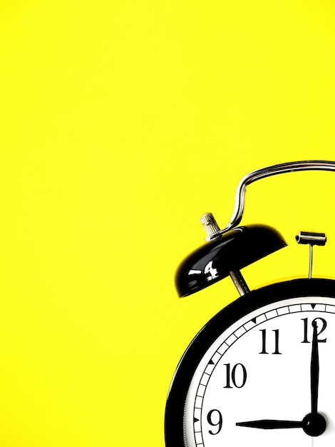 Black retro alarm clock at 9 nine o clock on a yellow background with copy space to add text 9am 9pm