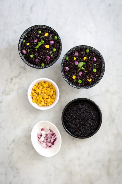 Black rice in a bowl and vegetables on marble table