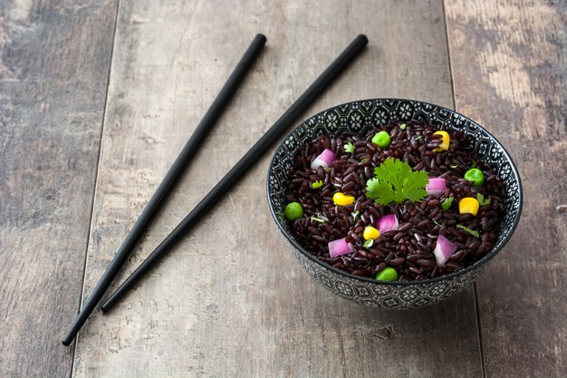 Black rice in a bowl and vegetables on wooden table. Copy space