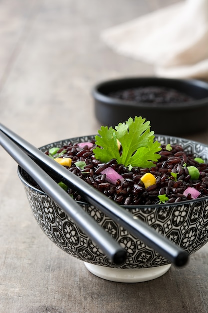 Foto riso nero in una ciotola e verdure sulla tavola di legno