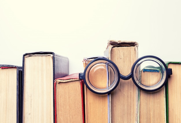 Black round glasses lay on top of a pile of battered old books.